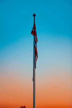 A flag on a pole silhouetted against a vibrant sunset sky, representing national pride.