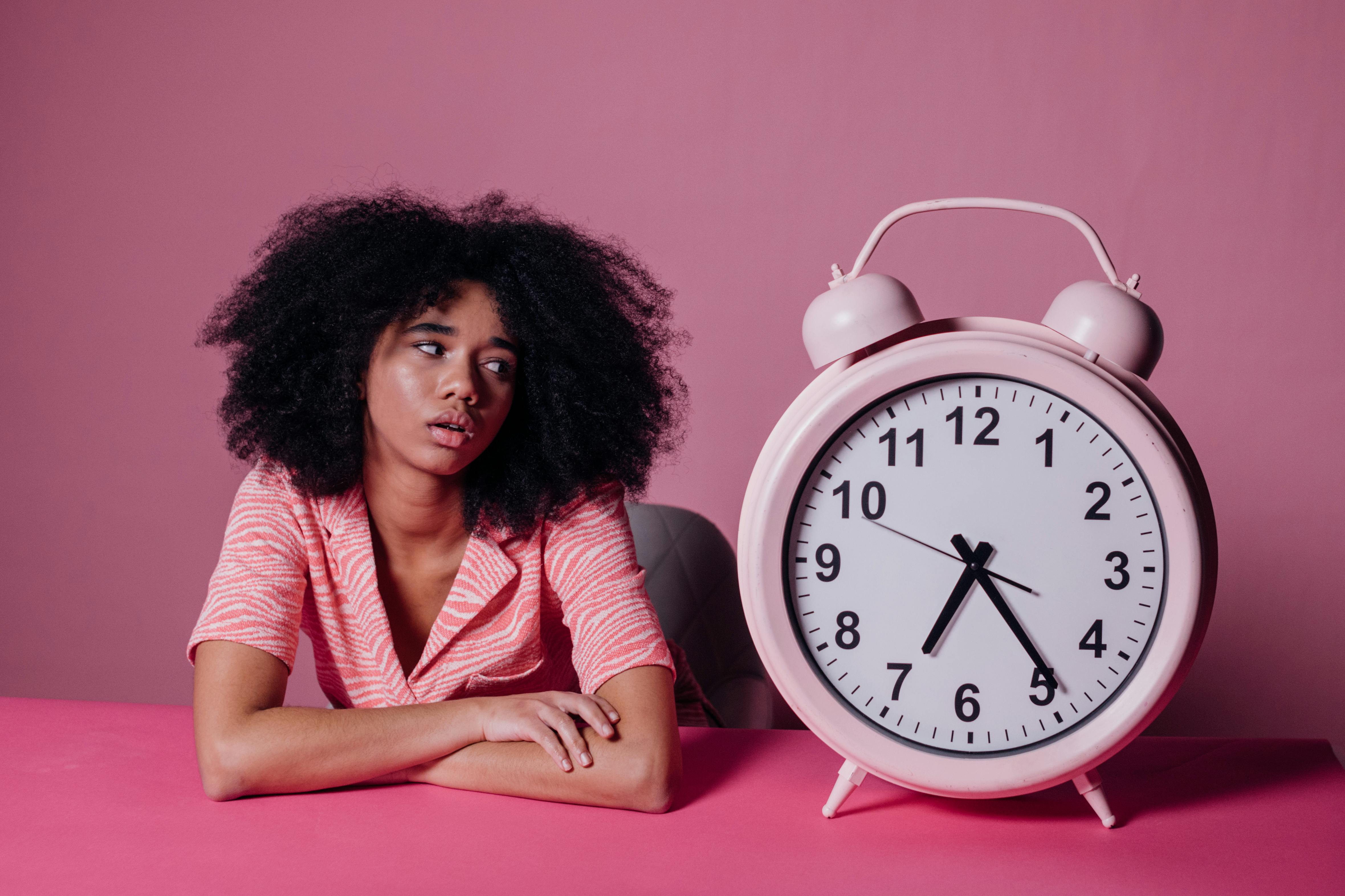 woman looking at a big pink alarm clock