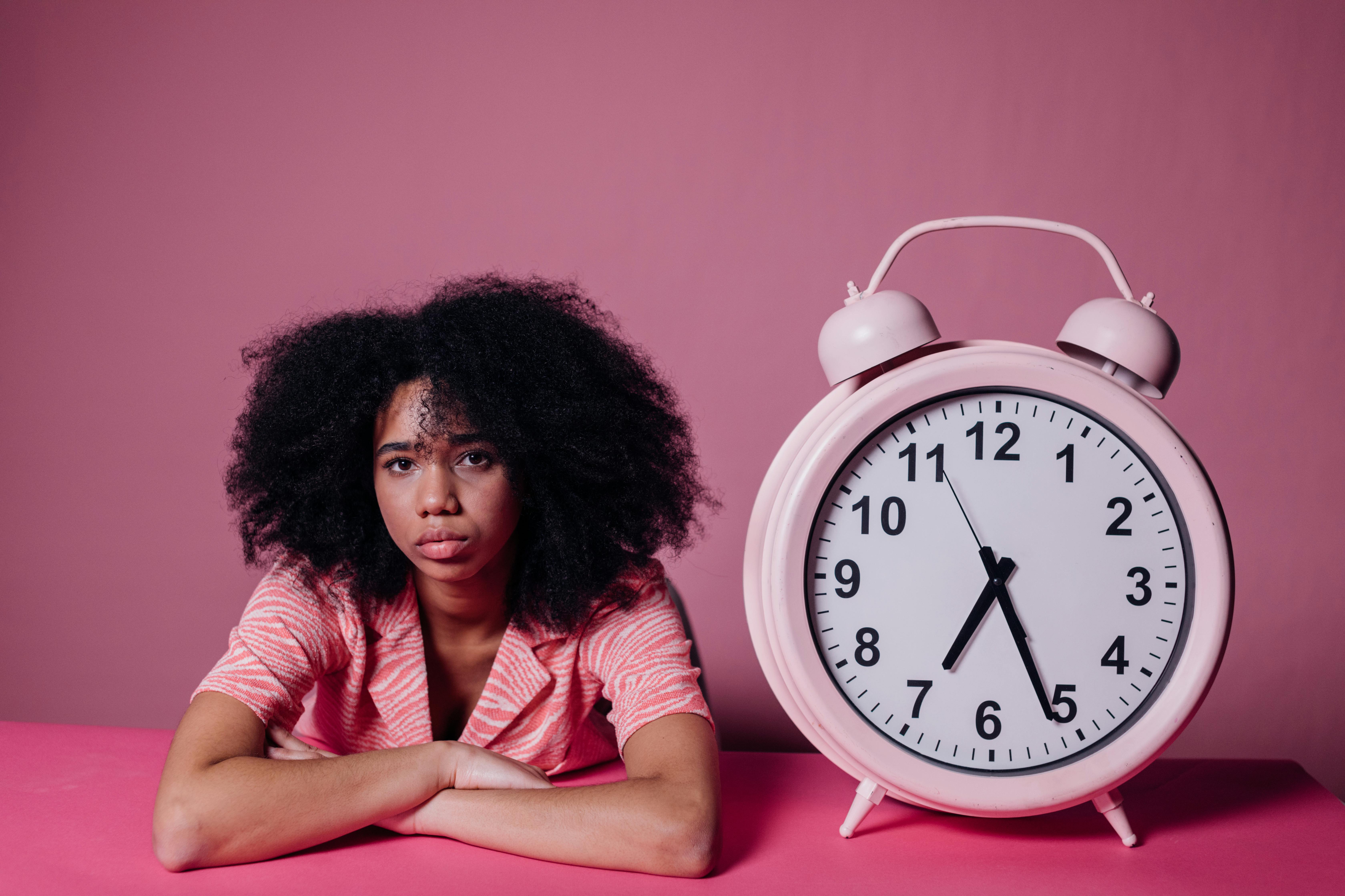 woman looking bored beside a big alarm clock