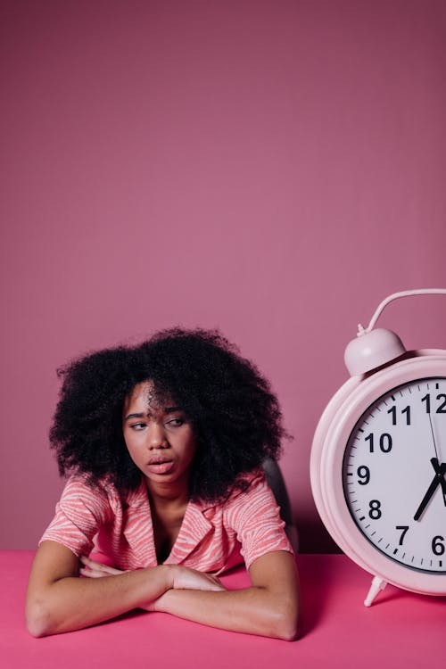 Free Woman Looking Bored Beside a Big Alarm Clock Stock Photo