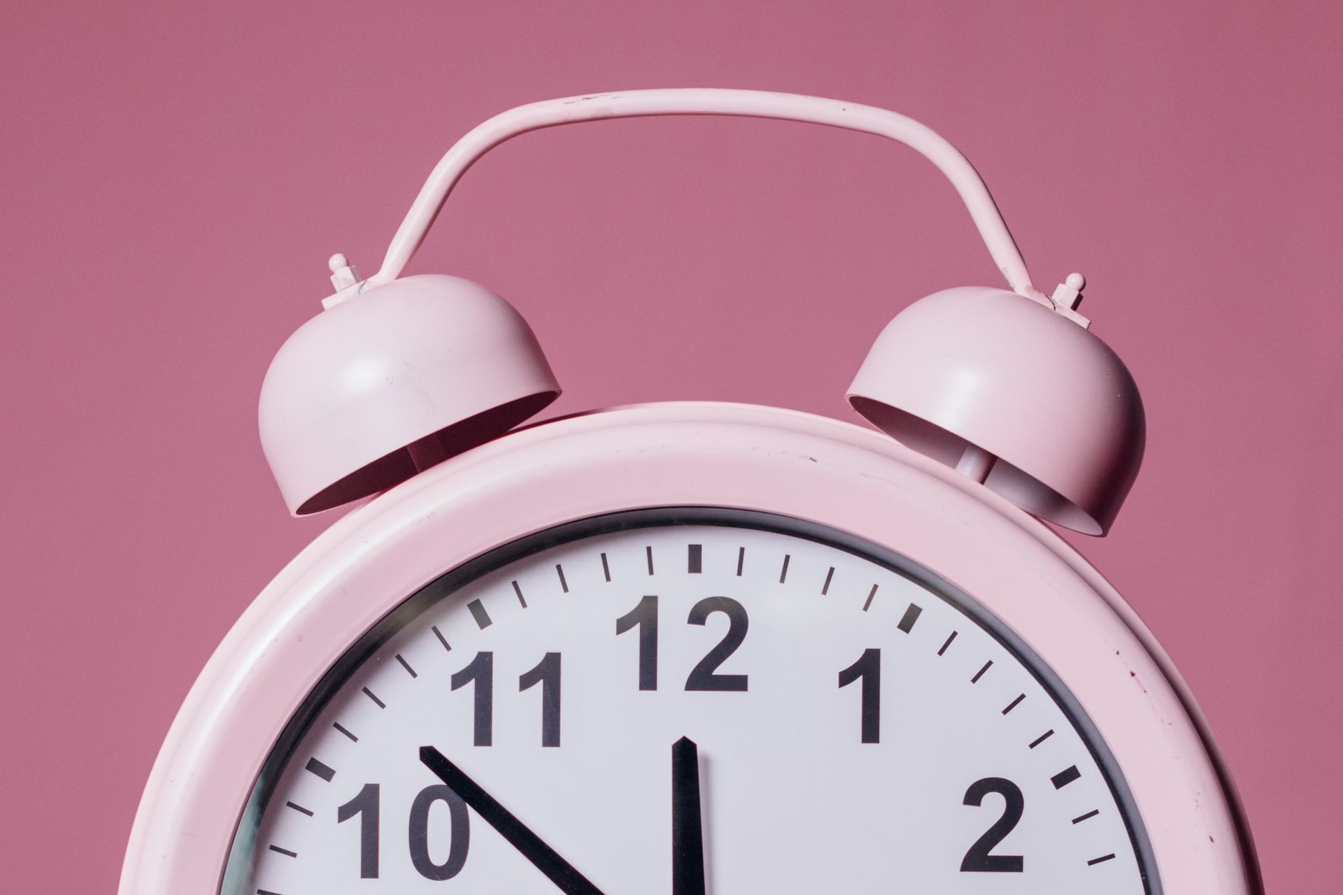 A close-up shot of a pastel pink alarm clock on a matching pink background, capturing the time with elegance.