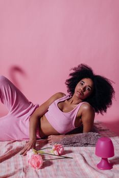 Portrait of a woman with afro hair posing on a pink backdrop, wearing a pink crop top and pants. Studio shot.