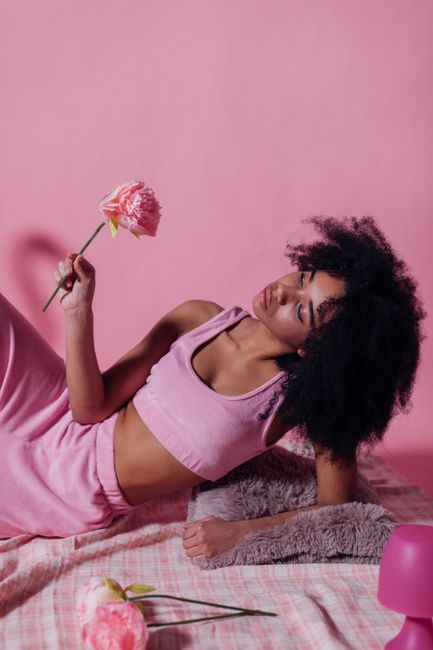 Studio portrait of an adult woman with afro hair holding a pink rose.