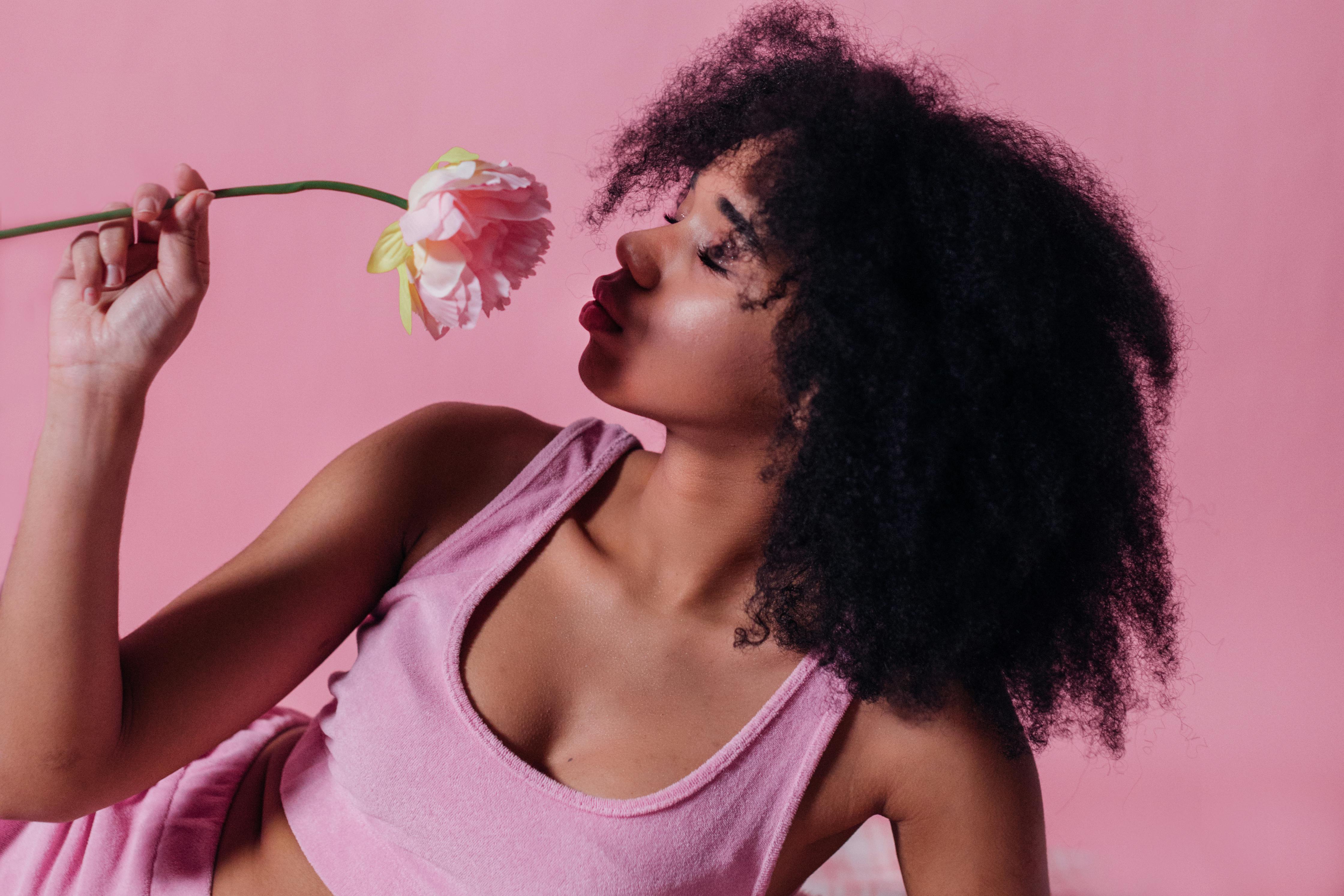 woman in pink crop top smelling a pink rose