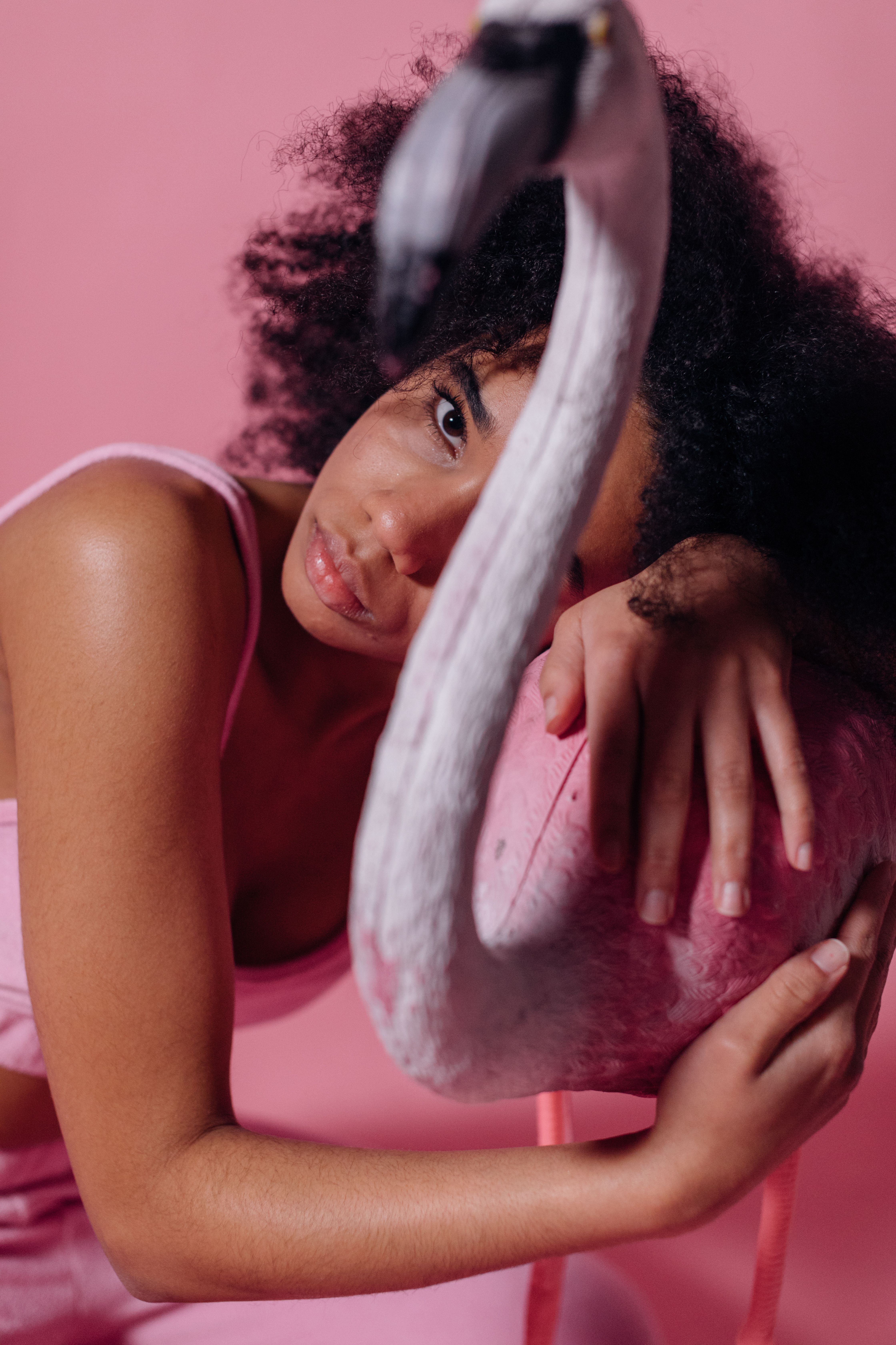 Close-up portrait of a black woman embracing a flamingo, set against a pink background for a vibrant aesthetic.