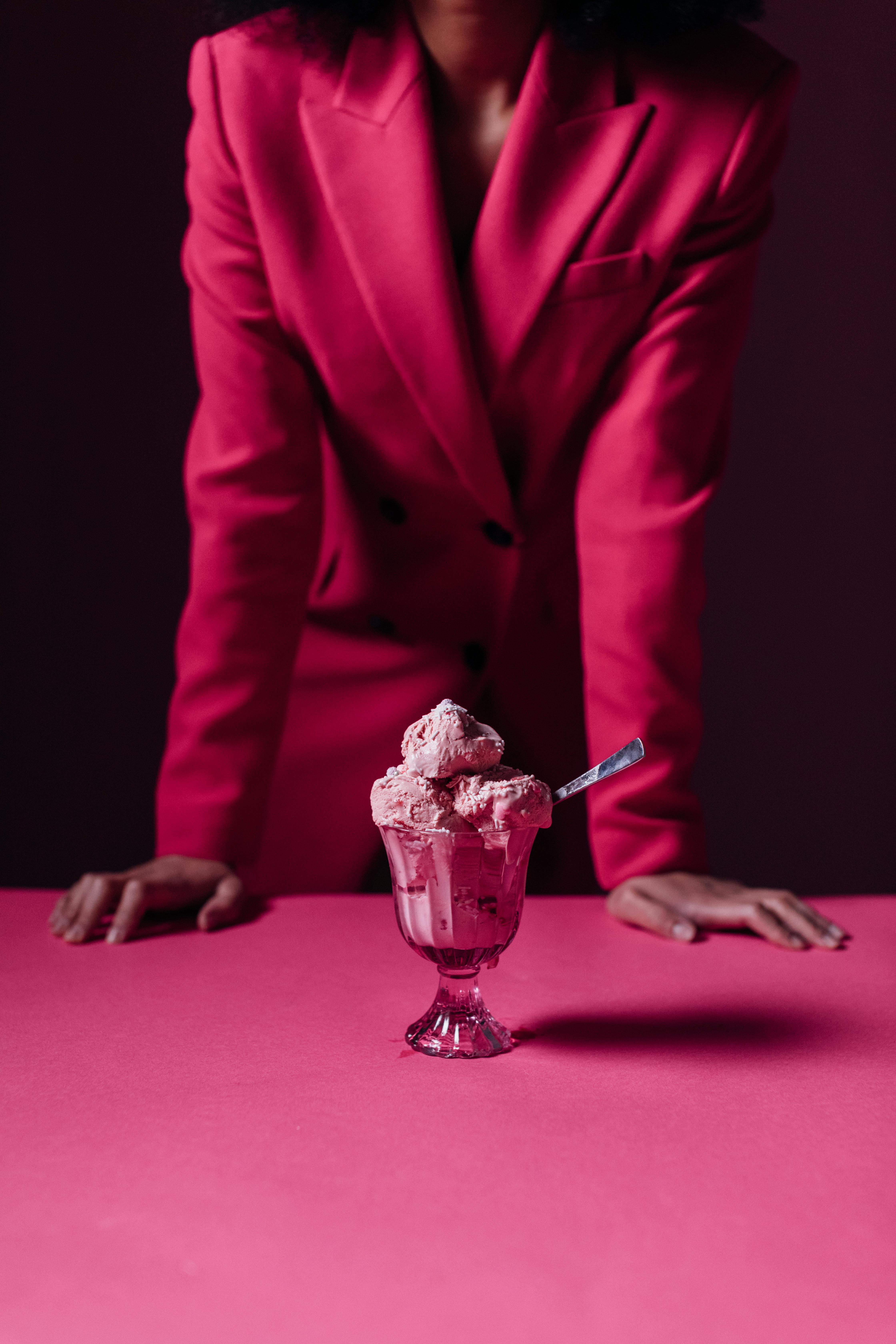 A chic ice cream dessert in a glass with a woman in a pink suit leaning over a matching table.