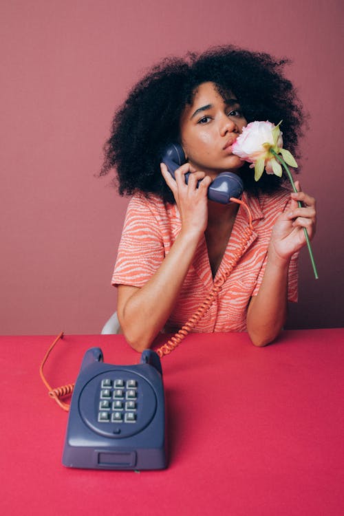 Free Woman Using an Old Telephone while Holding a Pink Rose Stock Photo