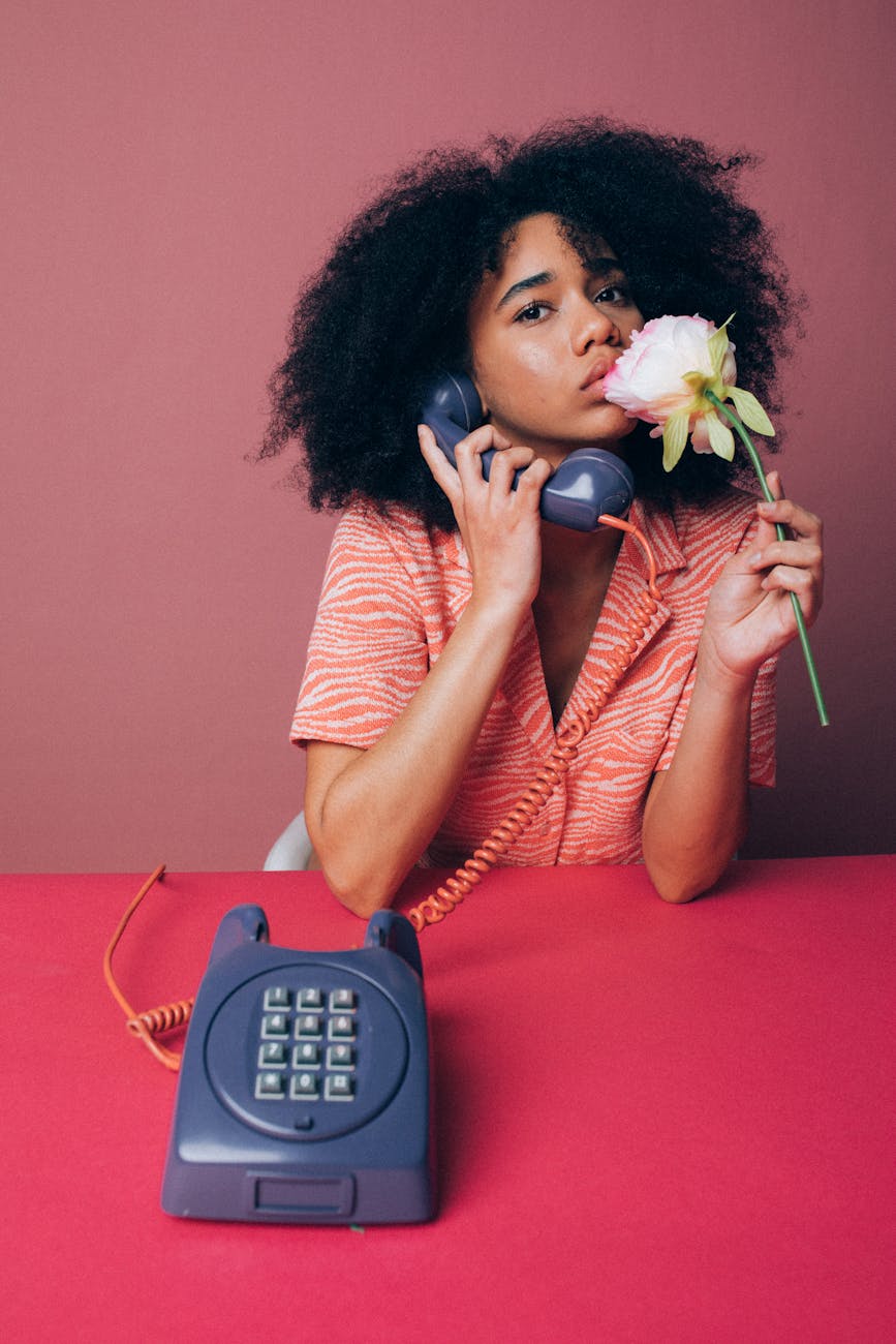 Portrait of a woman with afro hair holding a vintage telephone and pink rose.