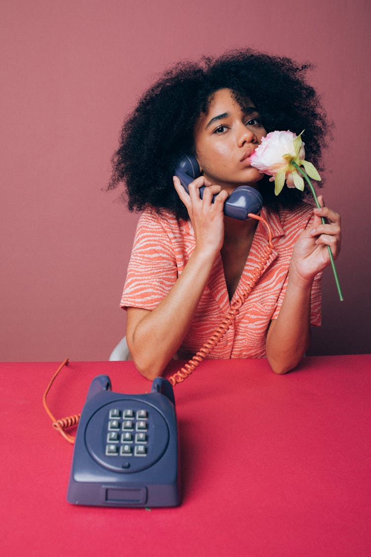 Woman Using An Old Telephone While Holding A Pink Rose