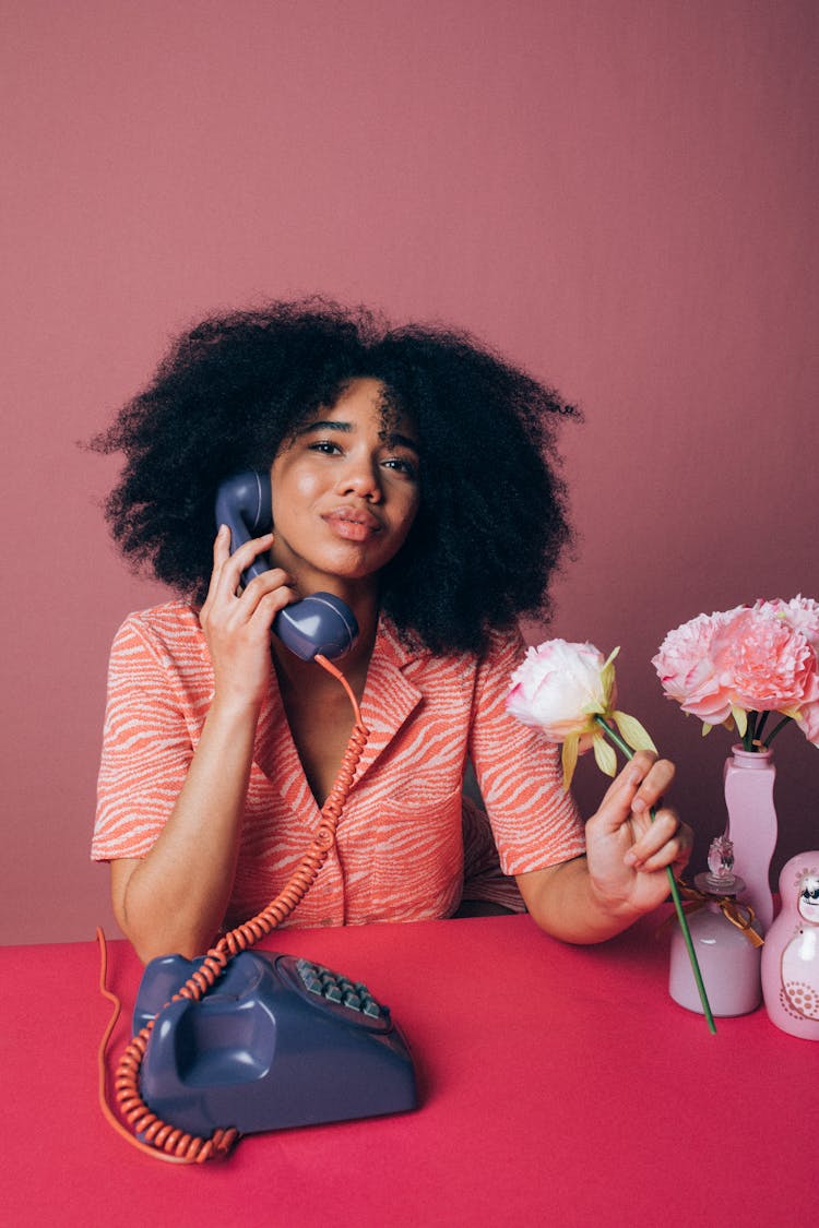 Woman Using An Old Telephone While Holding A Pink Rose