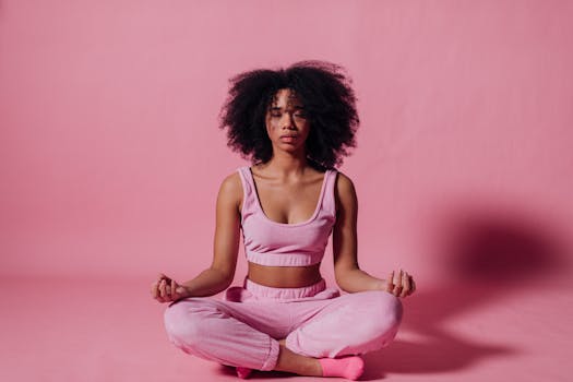 A woman with afro hair meditates in a peaceful studio with pink surroundings, embodying relaxation and zen.