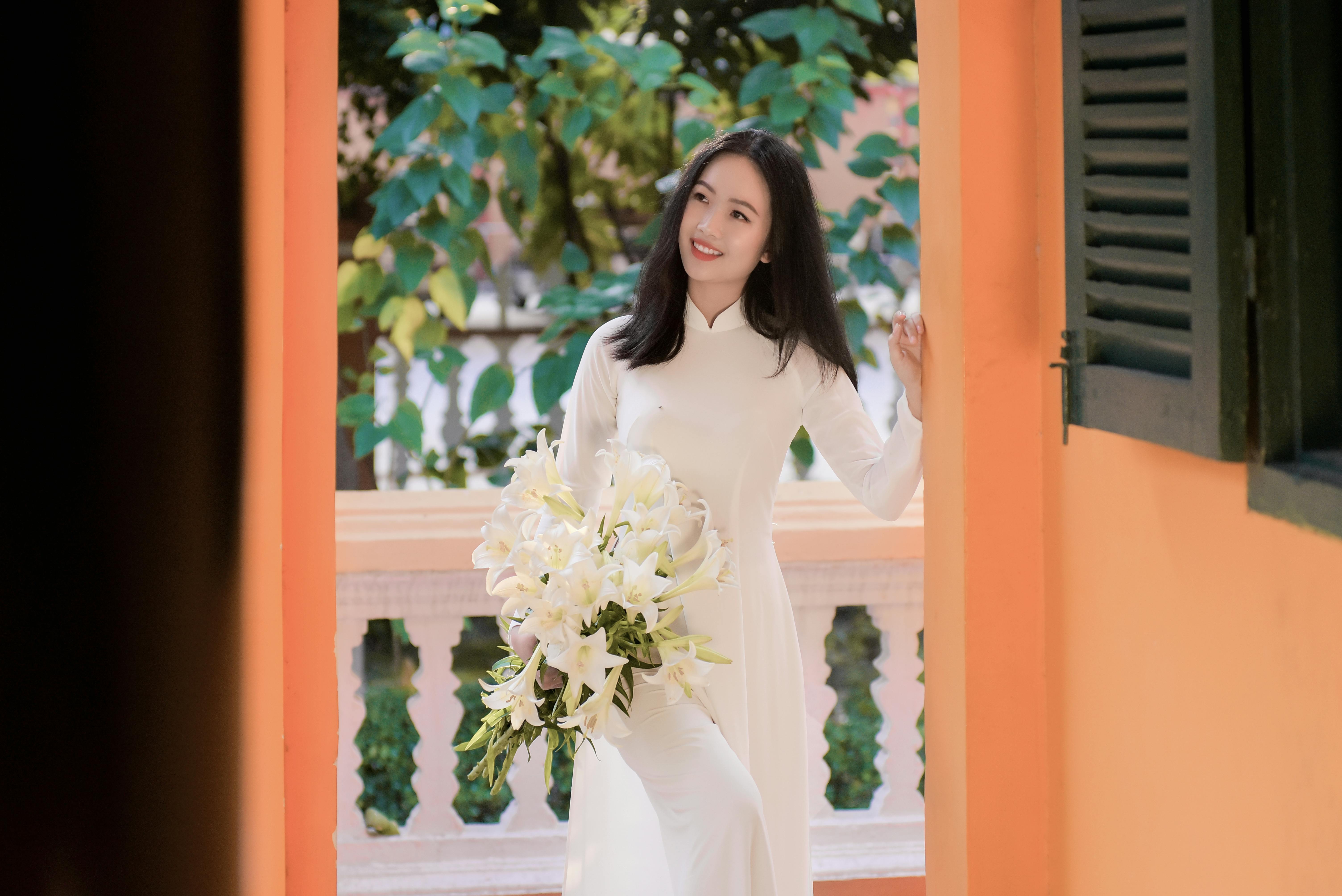 Woman in a White Dress Smiling while Holding Flowers
