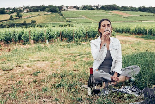 Woman in White Long Sleeve Shirt Sitting on Green Grass Field