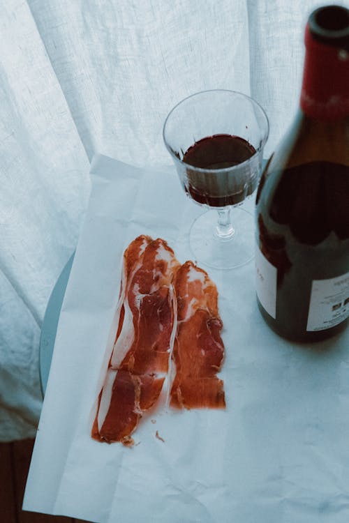 Photograph of a Bottle of Wine Beside Slices of Meat