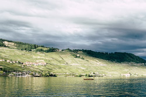 Free Green Mountain Beside Body of Water Under Cloudy Sky Stock Photo