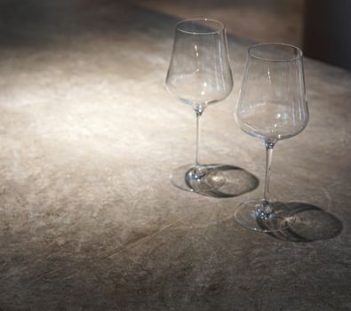 Two empty wine glasses casting shadows on a textured stone surface, suitable for dining themes.