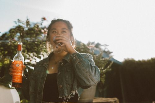 Free Asian woman sipping wine outdoors in Portugal, holding a bottle, wearing a denim jacket. Stock Photo