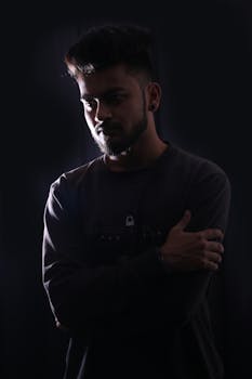 一个年轻人双臂交叉，站在阴影的灯光下，呈现出戏剧性的效果