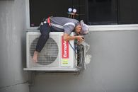 A technician skillfully repairing an outdoor air conditioning unit mounted on a building wall.
