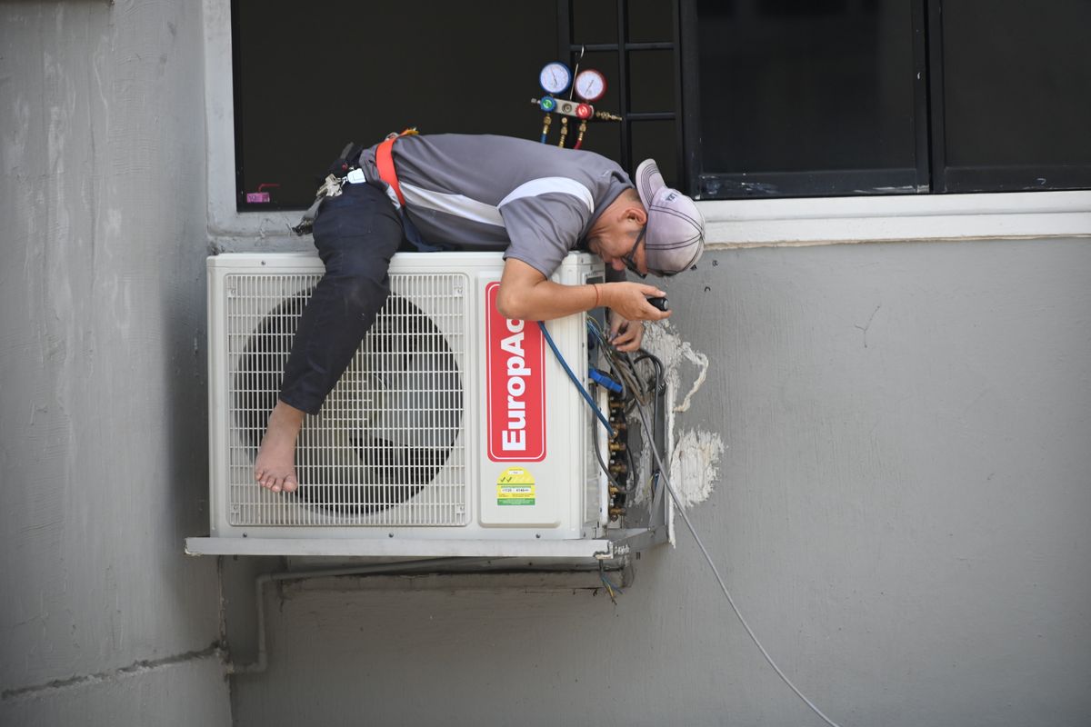 HVAC technician servicing an outdoor wall-mounted condenser unit, representative of licensed-trade plumbing and HVAC contractors financed through SBA 7(a) loans