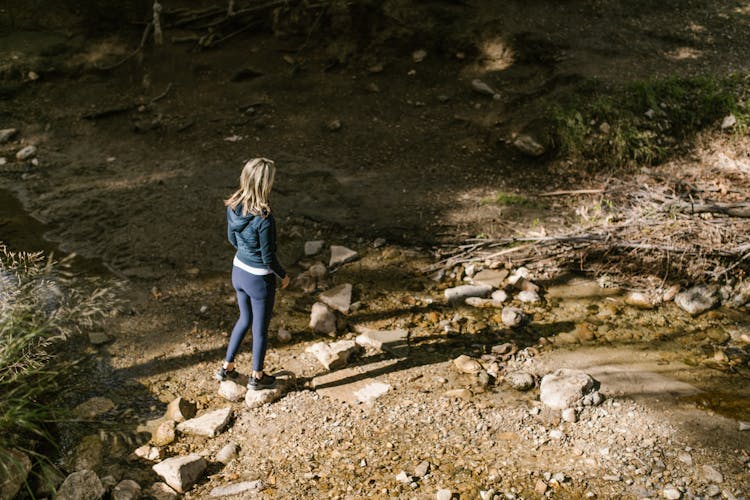 Woman Wearing Blue Hoodie And Leggings Standing On Rocks On Dirt Ground