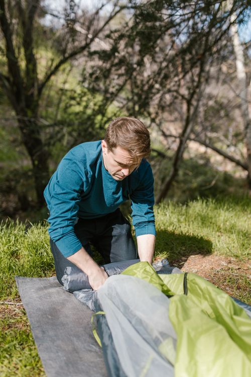 Free A man assembling a tent in a sunlit forest setting, perfect for camping enthusiasts. Stock Photo