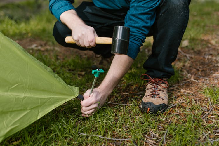 A Person Hammering A Tent Peg On The Ground