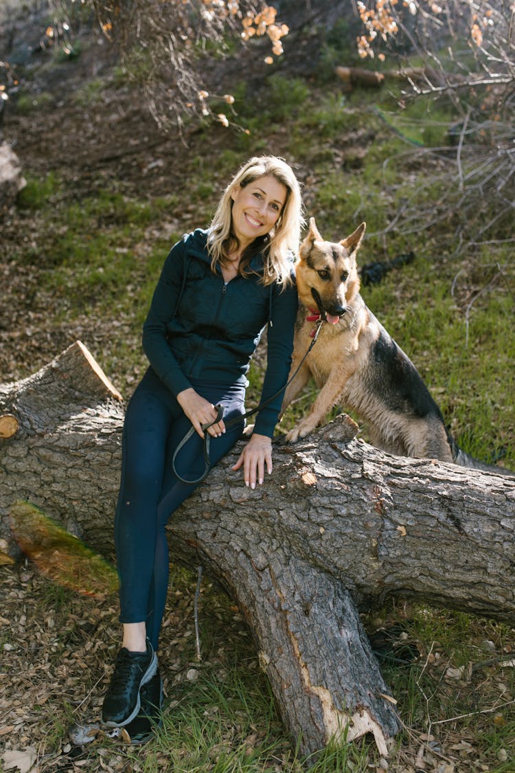 A Woman Sitting On A Tree Trunk With Her Pet German Shepherd