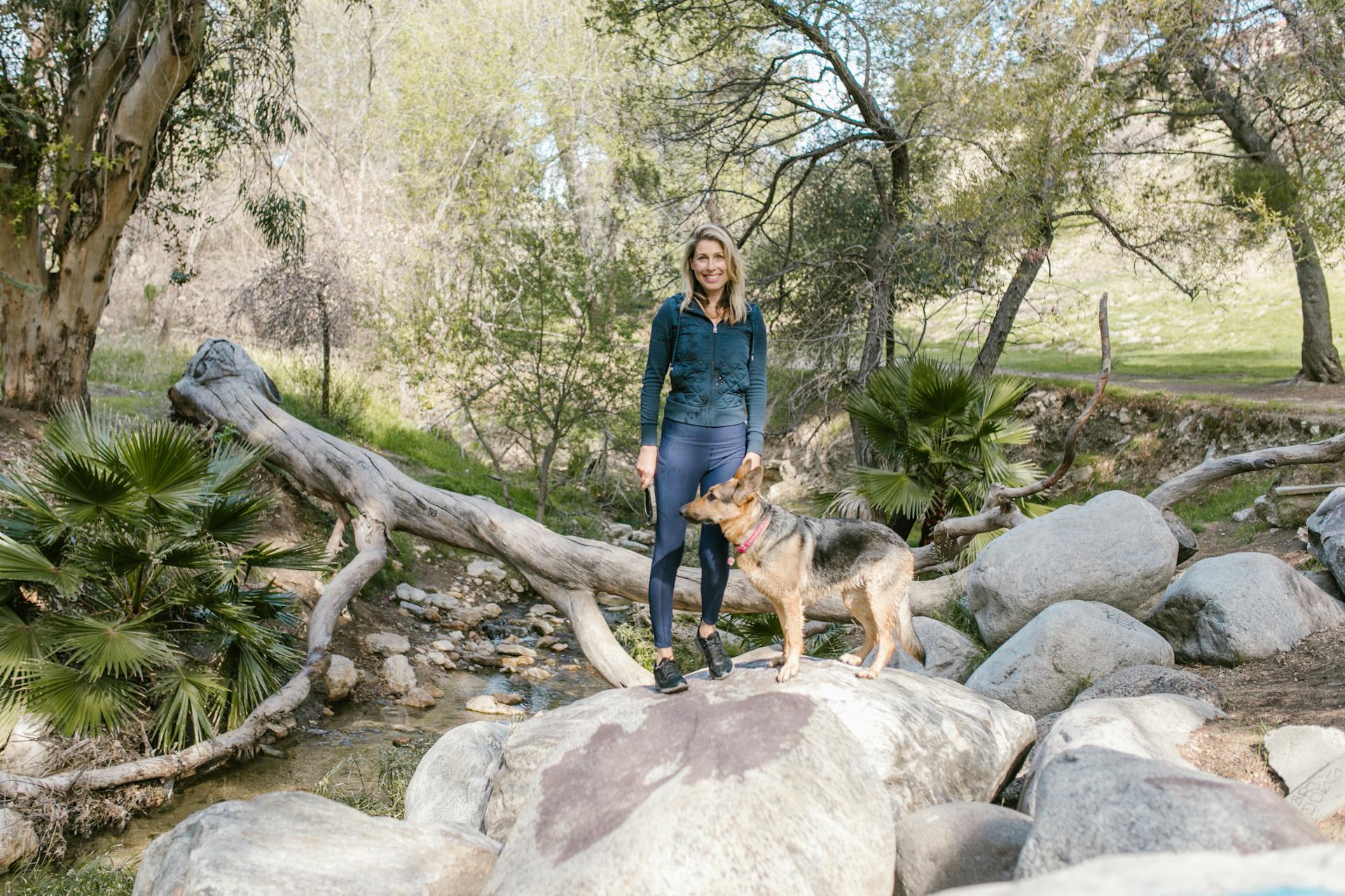 A Woman in Blue Jacket and Leggings Standing on the Rock Beside Her Dog