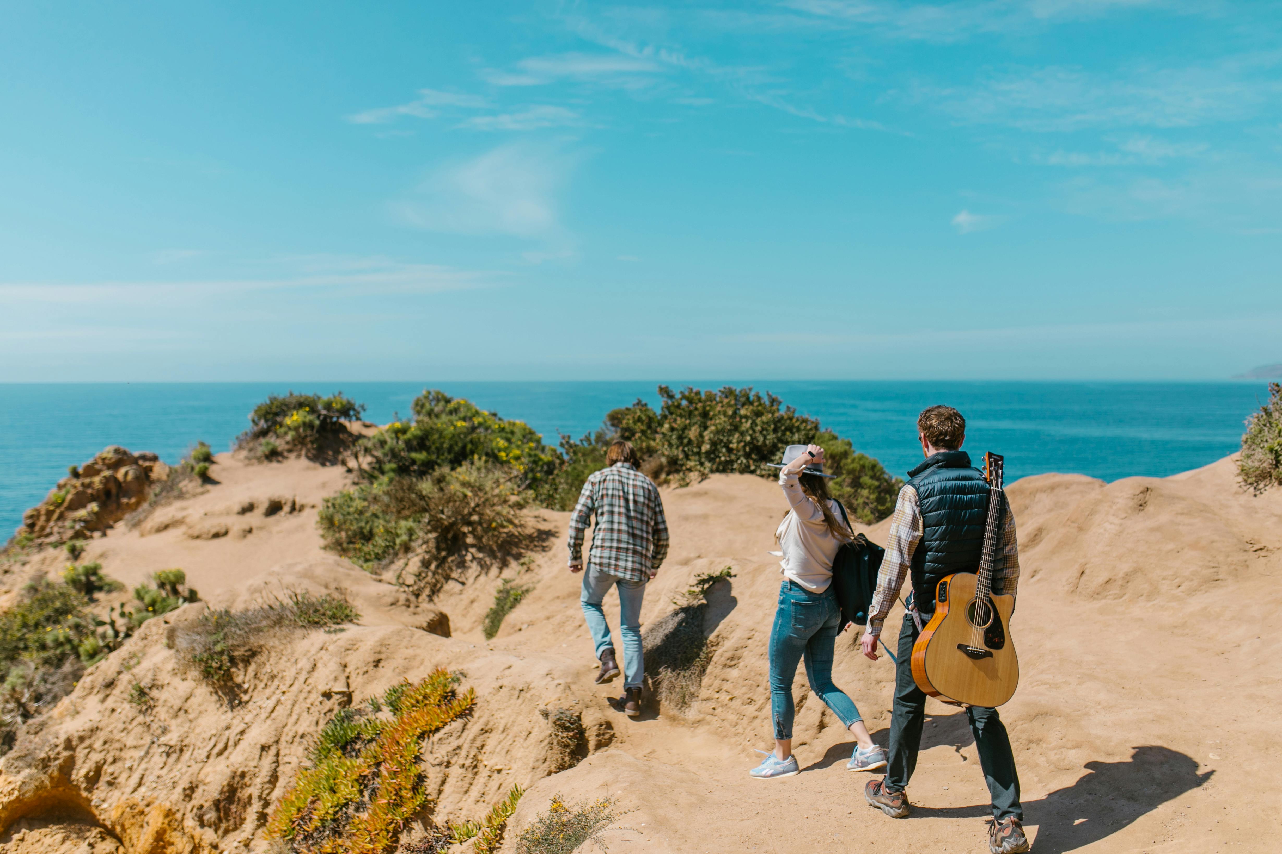 A group enjoying a scenic coastal hike with a guitar under clear skies.