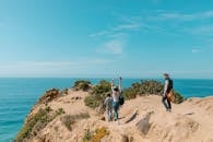 2 Women Standing on Brown Rock Formation Near Body of Water