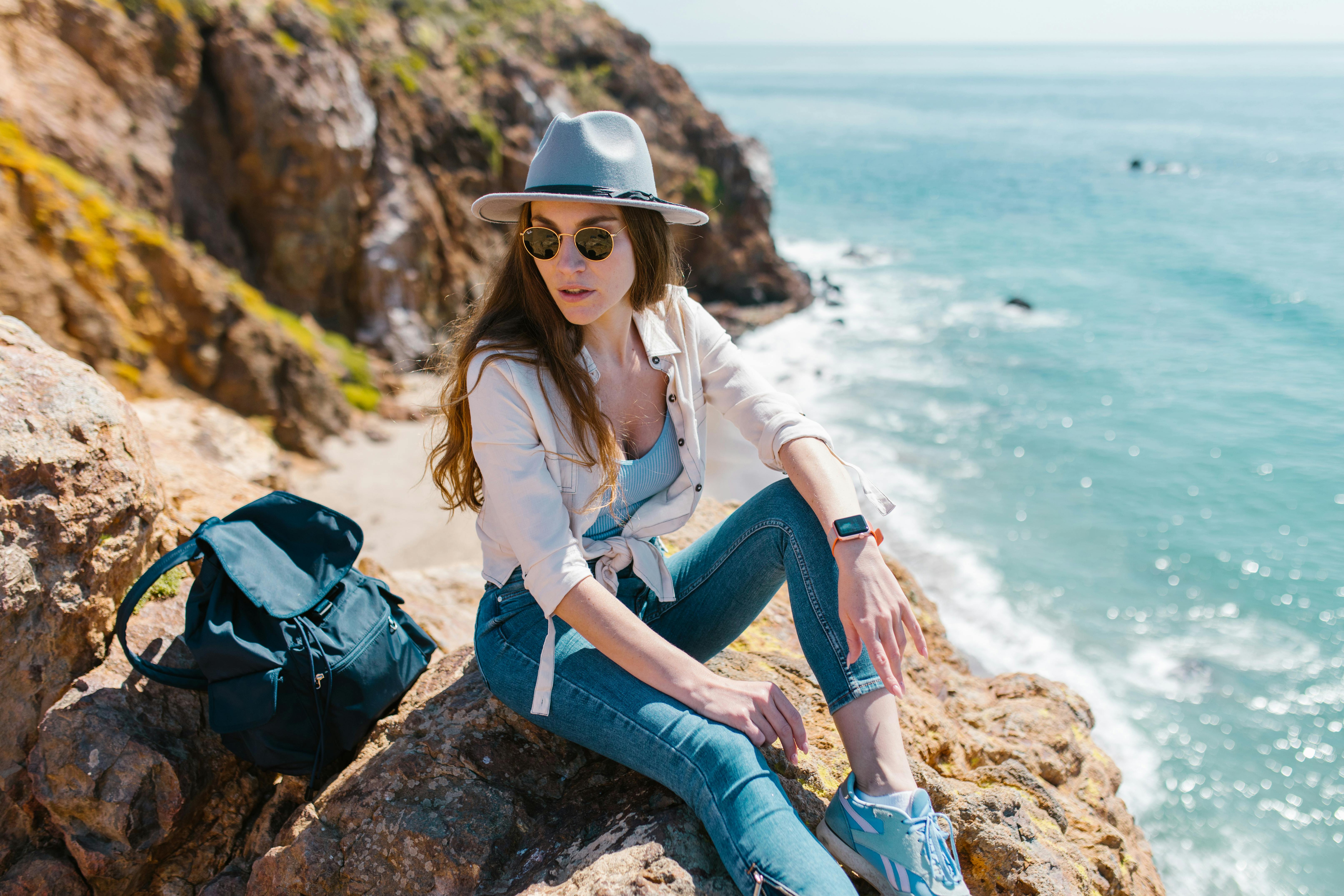 [ColoSach]-woman-in-casual-fashion-sitting-on-cliffs-by-the-ocean,-embodying-summer-adventure-and-travel-vibes.