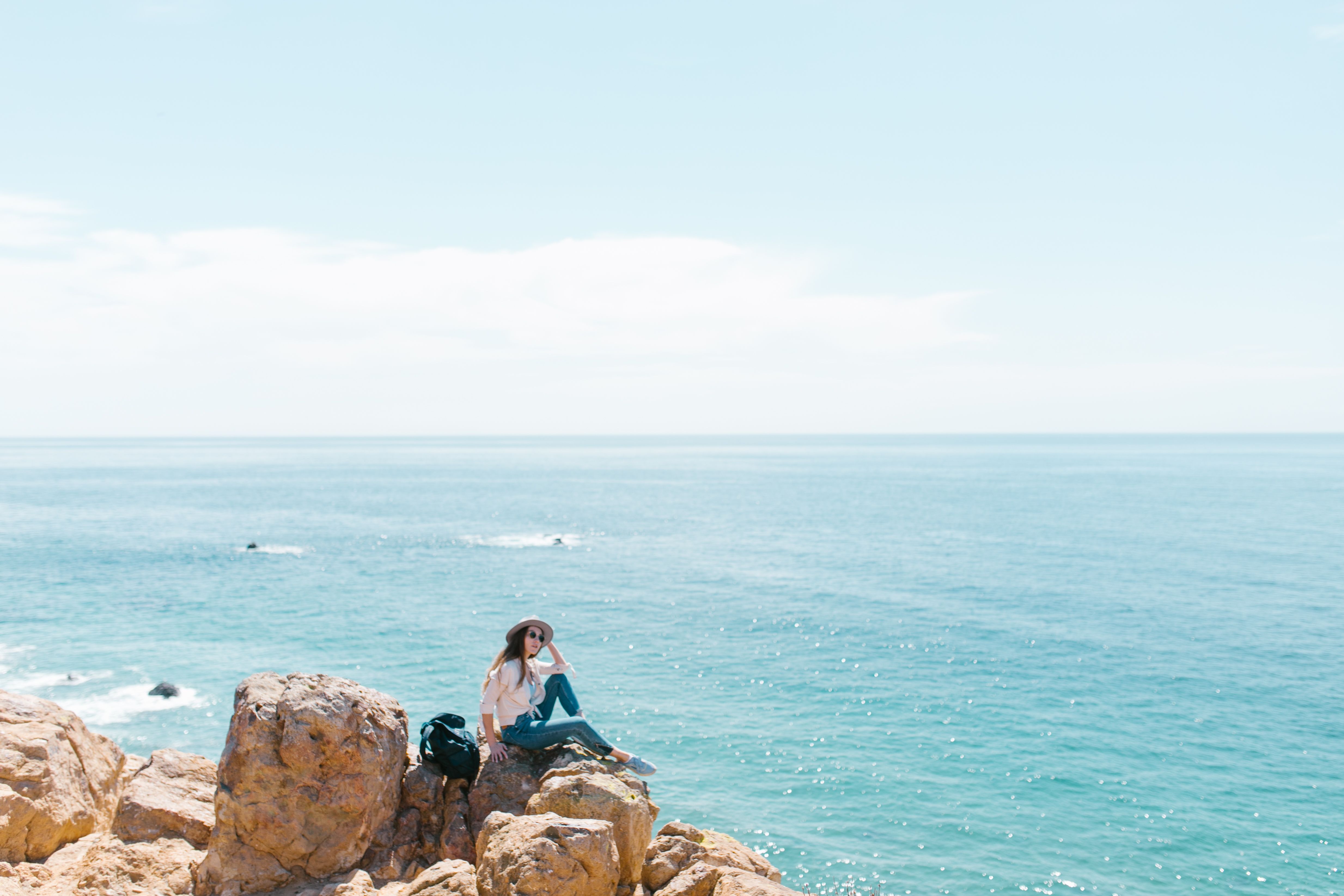 traveler sitting alone on a cliff overlooking ocean, contemplating