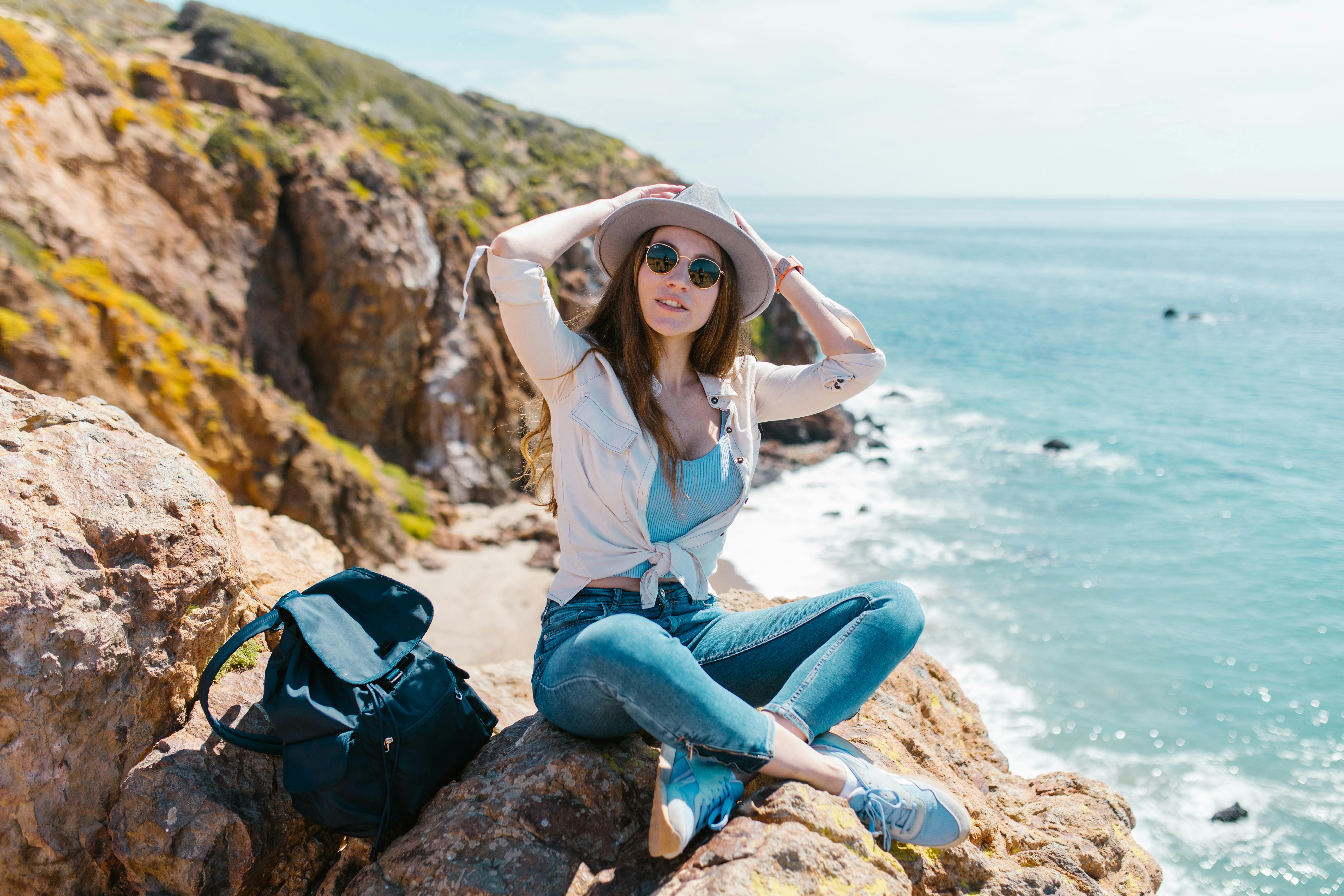 woman in white shirt and blue denim jeans sitting on rock near sea