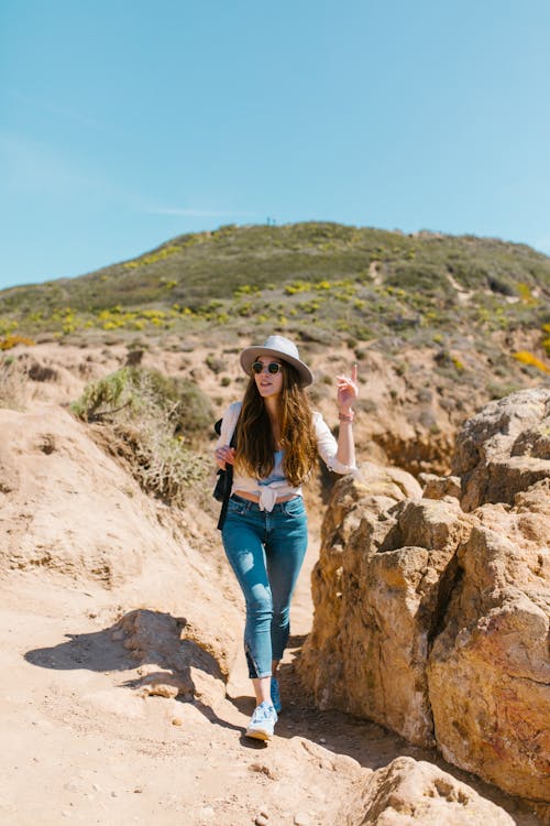 Photo of a Woman with Sunglasses Walking Beside a Rock