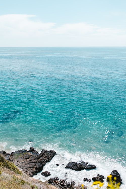 Free A breathtaking aerial view of a rocky coastline meeting the serene ocean under a clear sky. Stock Photo