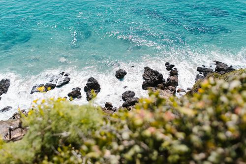 Free High-angle view of a rocky coastline with vibrant blue ocean waves gently crashing against the shore. Stock Photo