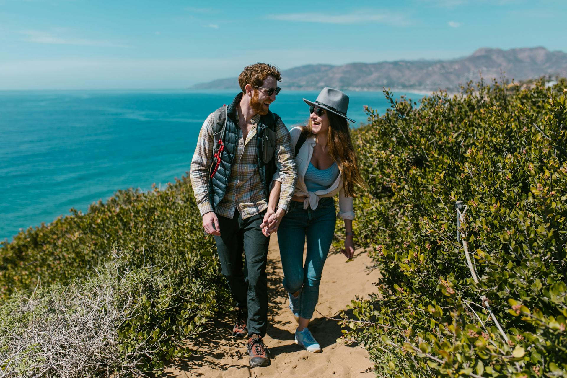 Happy couple holding hands while hiking on a scenic coastal trail with ocean views.