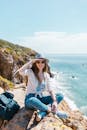 年轻女子坐在海边的悬崖上，在户外享受阳光明媚的一天
