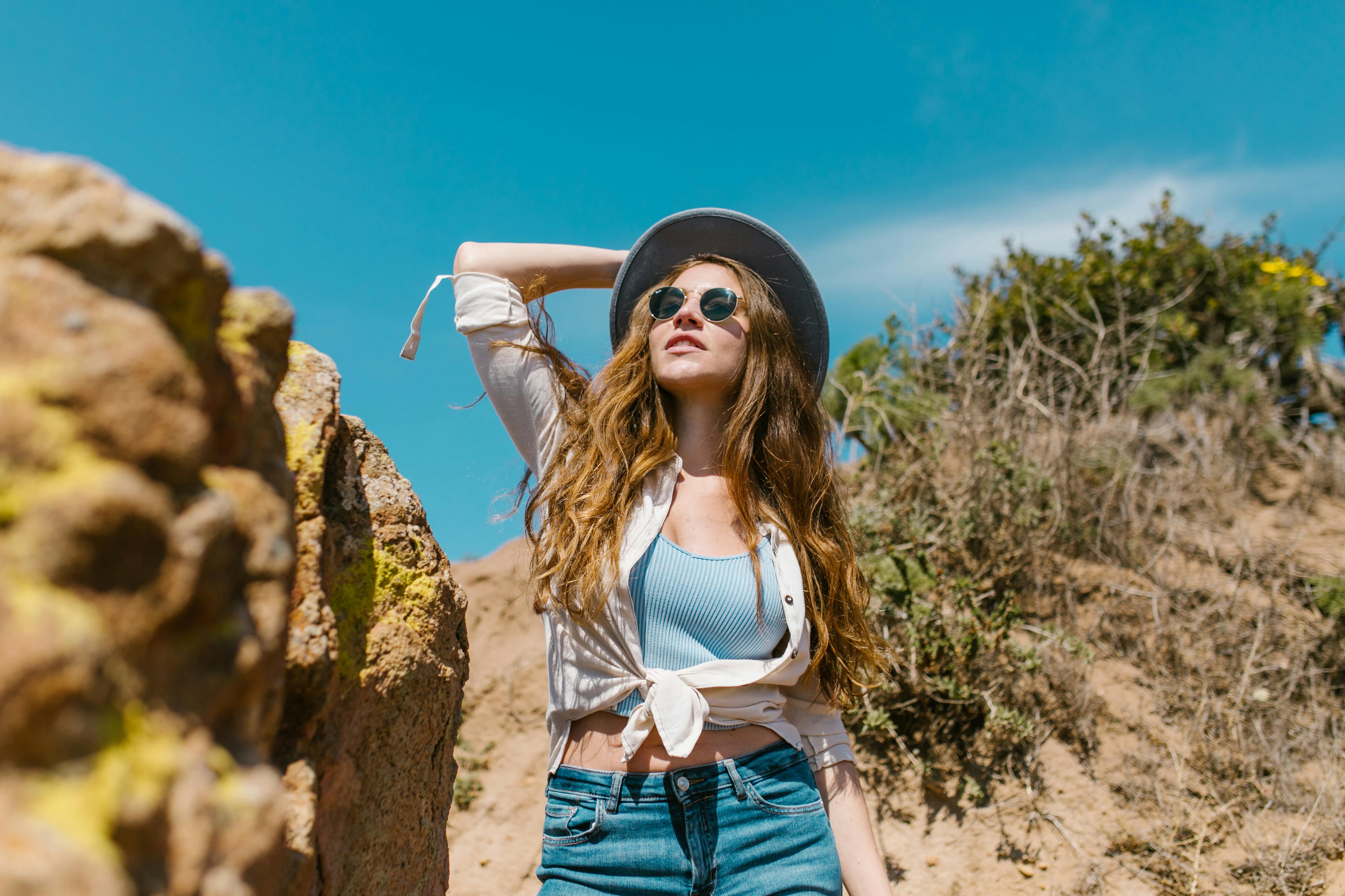 woman in white tank top and blue denim shorts standing on brown rock
