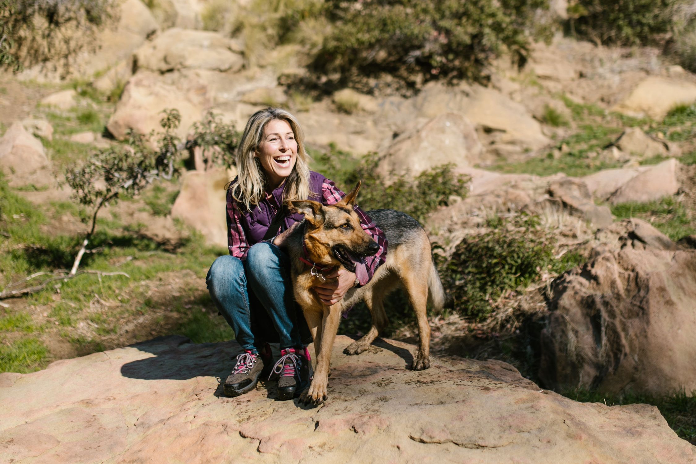 Smiling woman sitting with her German Shepherd during a hike in nature.