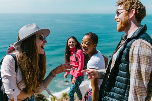 Group of friends laughing and talking by the ocean on a sunny day.
