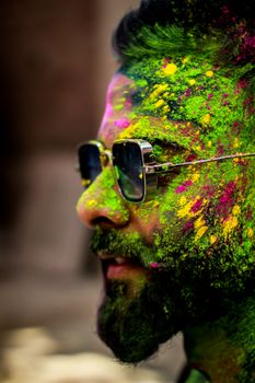 Close-up of a man celebrating Holi with vibrant colors in Patna, India, wearing sunglasses.