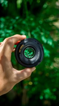 Close-up of a hand holding a lens, focusing on nature through the camera lens, with a vibrant green background.
