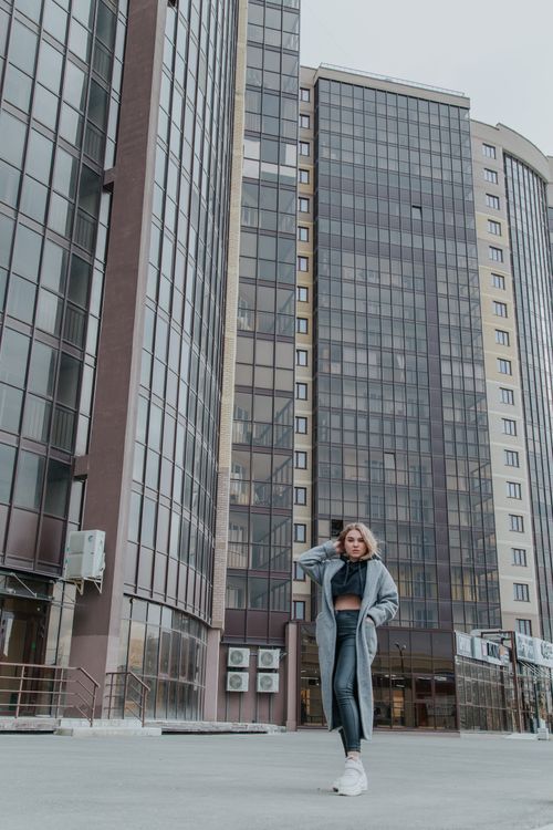 Free Full body of young female in trendy outfit standing near contemporary multistory residential houses with glass walls on street in city Stock Photo