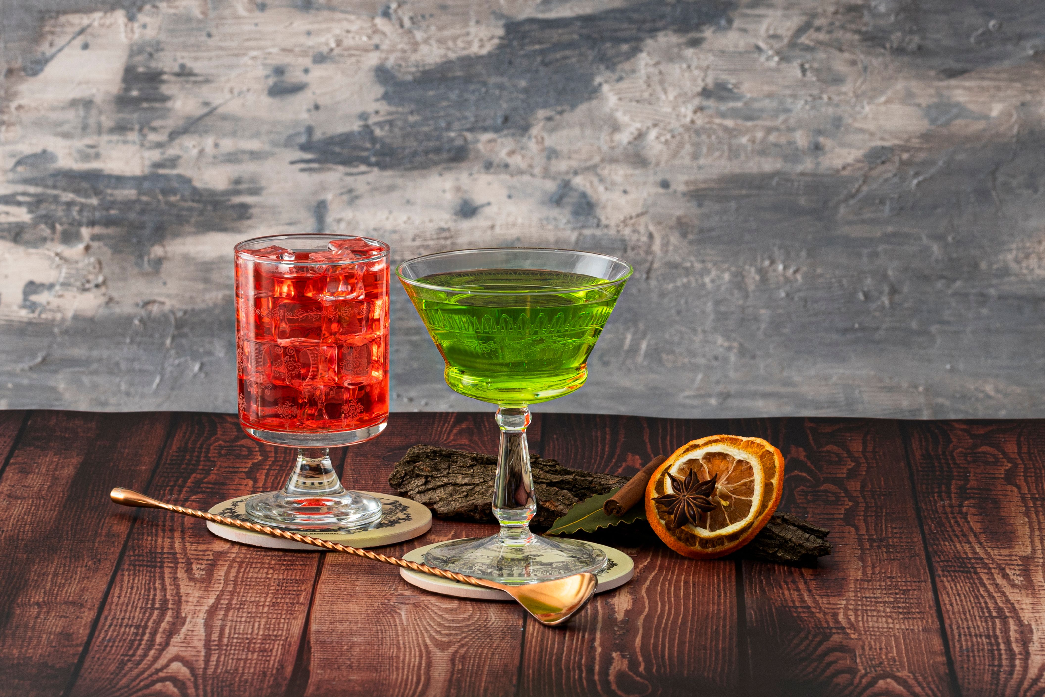 Colorful red and green cocktails on a rustic wooden table with citrus garnish.