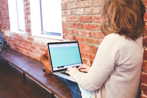 Free Woman Using Macbook While Sitting on Brown Wooden Bench Stock Photo