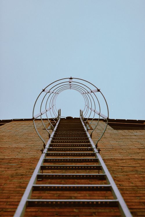 Free Low-angle shot of a metal emergency exit ladder against a brick wall. Stock Photo