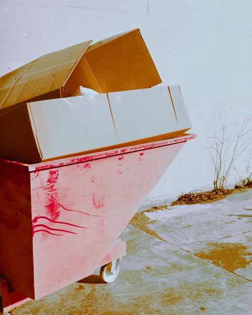 A red dumpster filled with cardboard boxes outside against a white wall in Trondheim.