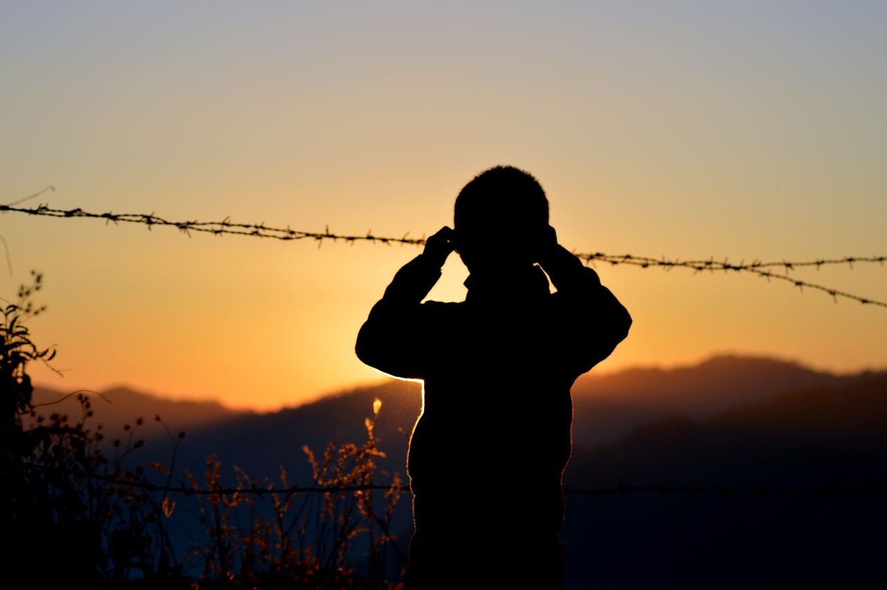 a silhouette of a child looking through barbed wire at the sunset in s